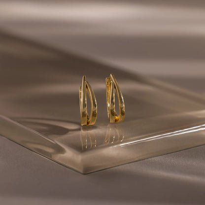 Gold hoop earrings on a reflective brown surface