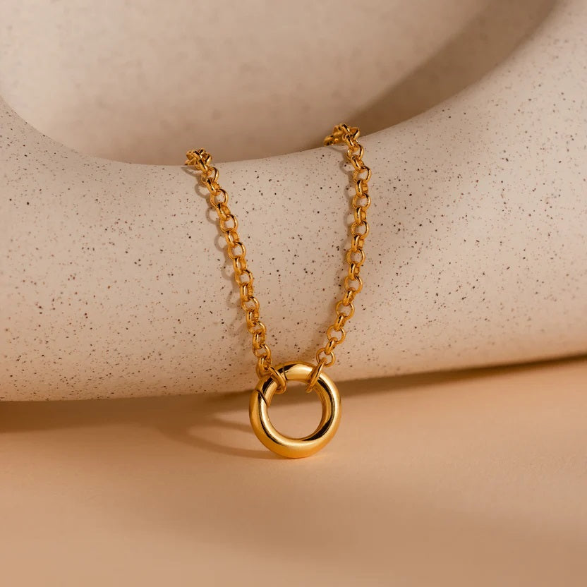 Gold necklace with a circular pendant on a beige surface
