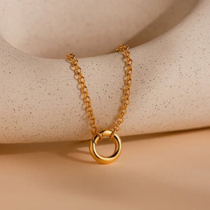 Gold necklace with a circular pendant on a beige surface