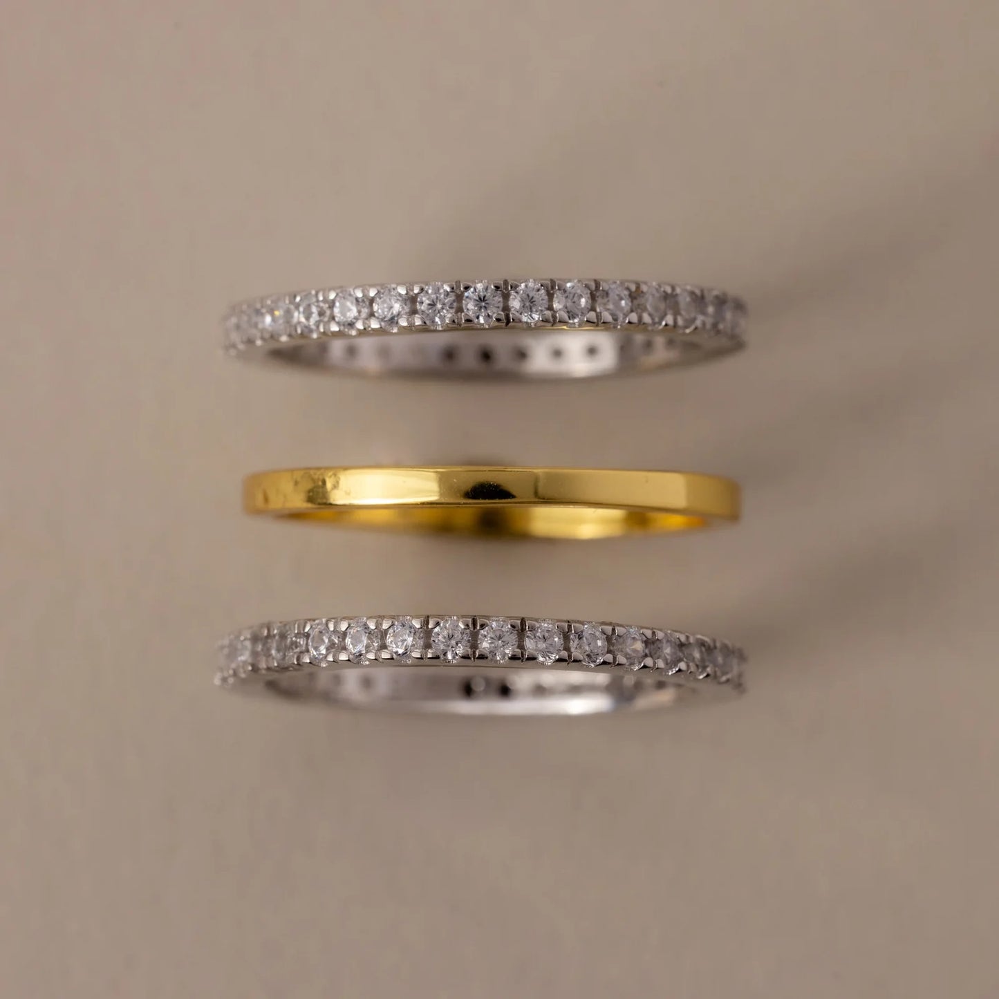 Three diamond-studded rings on a beige background