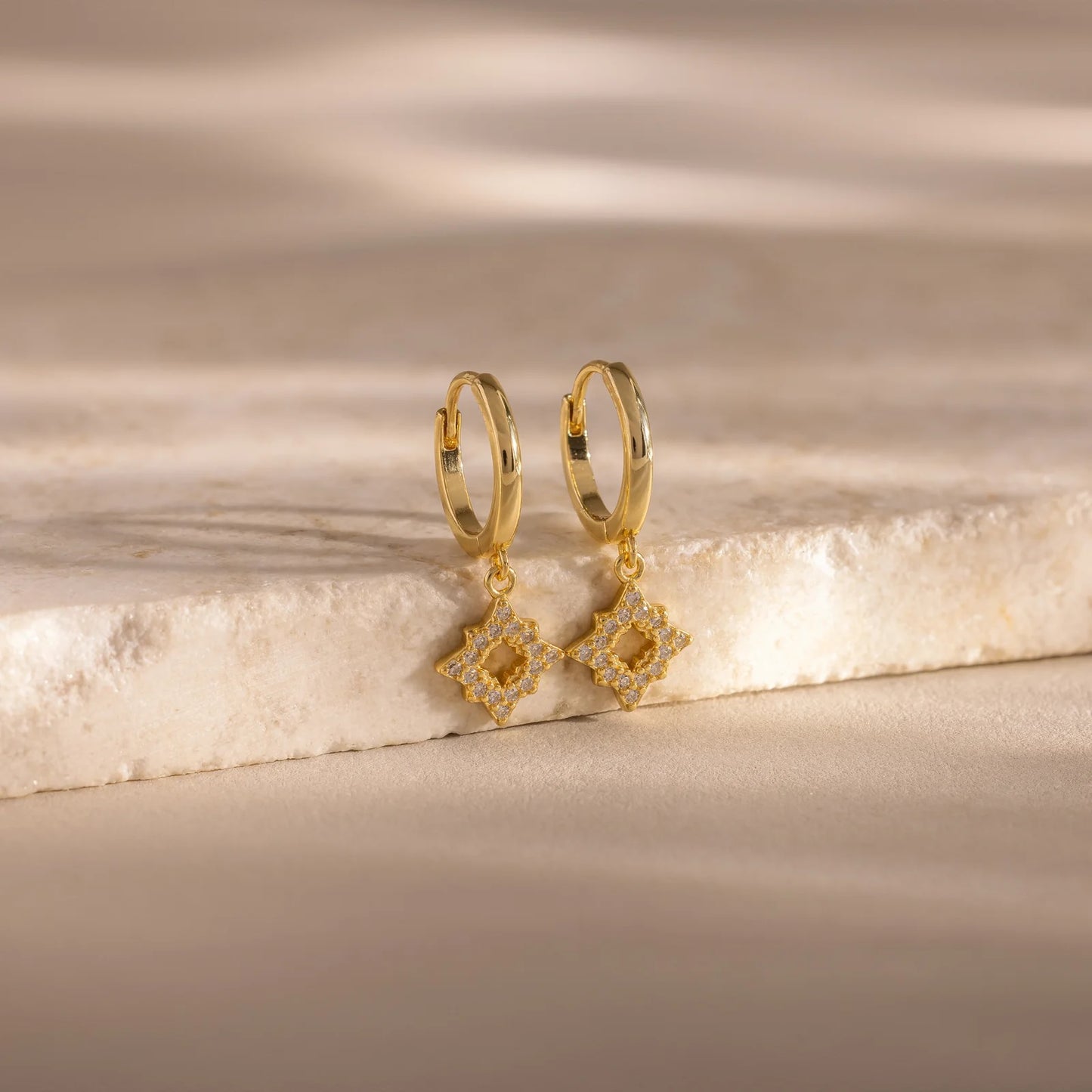 Gold hoop earrings with diamond-shaped drops on a marble surface