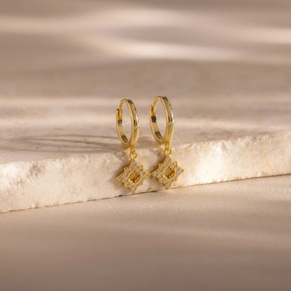 Gold hoop earrings with diamond-shaped drops on a marble surface
