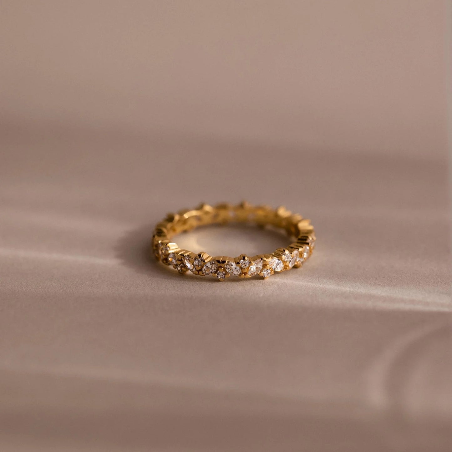 Gold ring with embedded diamonds on a beige fabric background