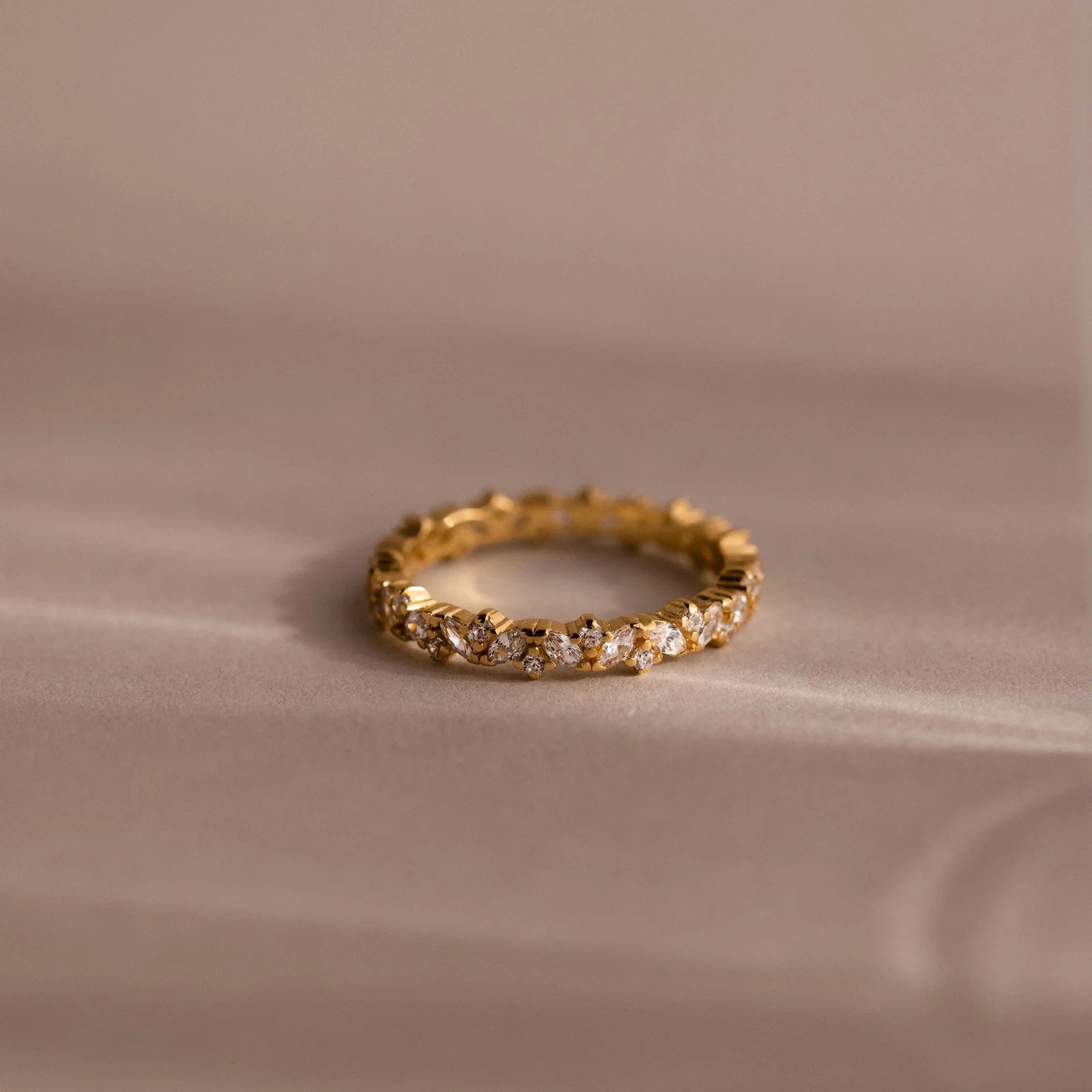 Gold ring with embedded diamonds on a beige fabric background