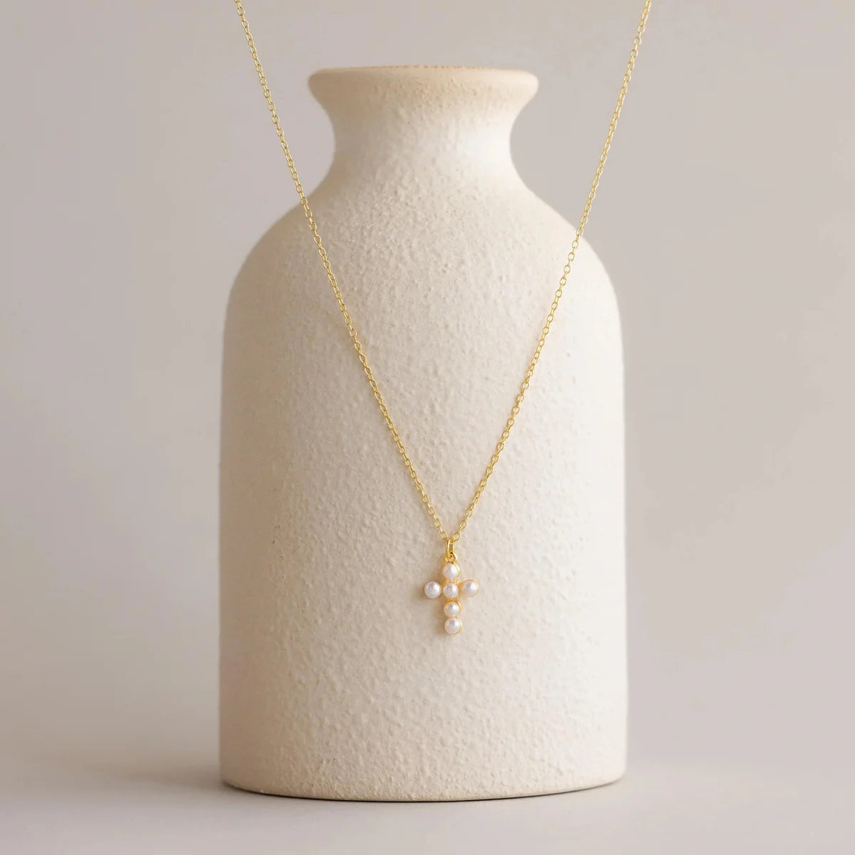 Gold necklace with a cross pendant on a textured white vase against a light background