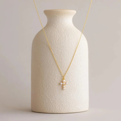 Gold necklace with a cross pendant on a textured white vase against a light background