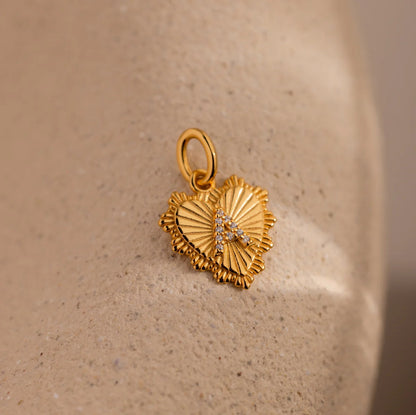 Gold heart-shaped pendant with letter 'A' on a beige stone surface