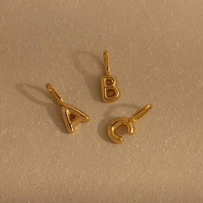 Three gold letter pendants (A, B, C) on a beige background