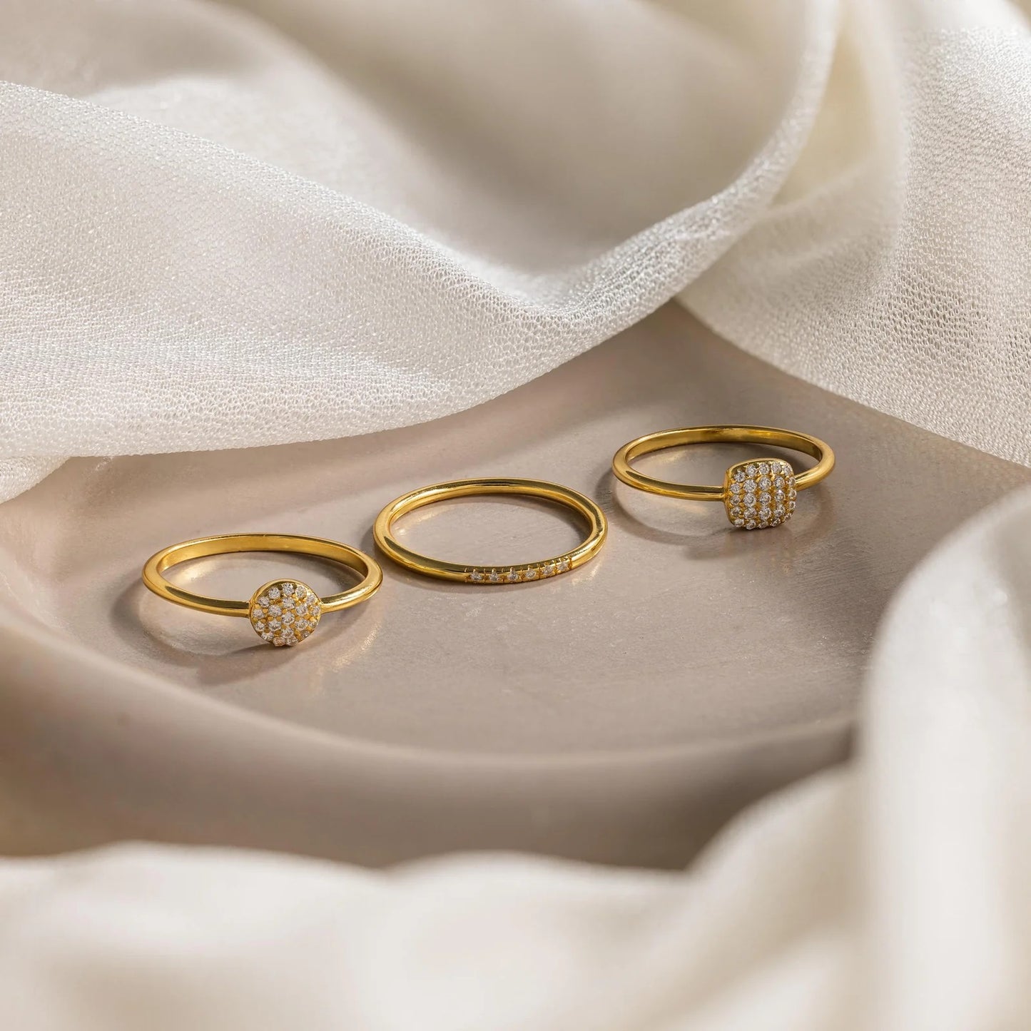 Three gold rings with diamond accents on a soft fabric background
