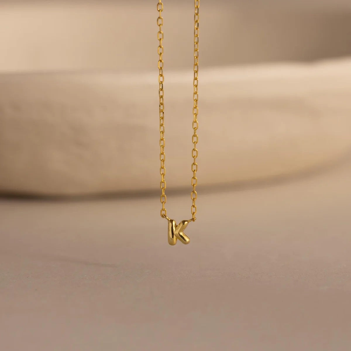 Gold necklace with a 'K' pendant on a beige background