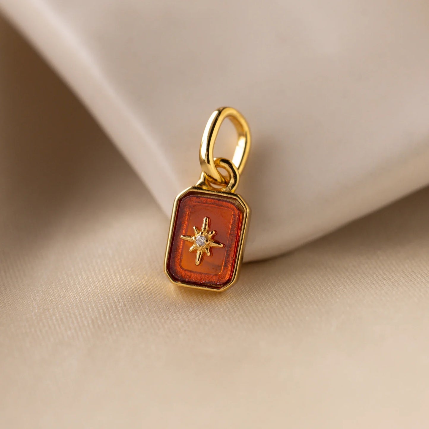 Gold pendant with a star design on an orange background, placed on beige fabric.