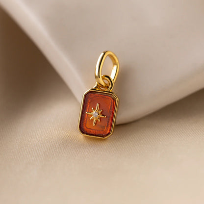 Gold pendant with a star design on an orange background, placed on beige fabric.