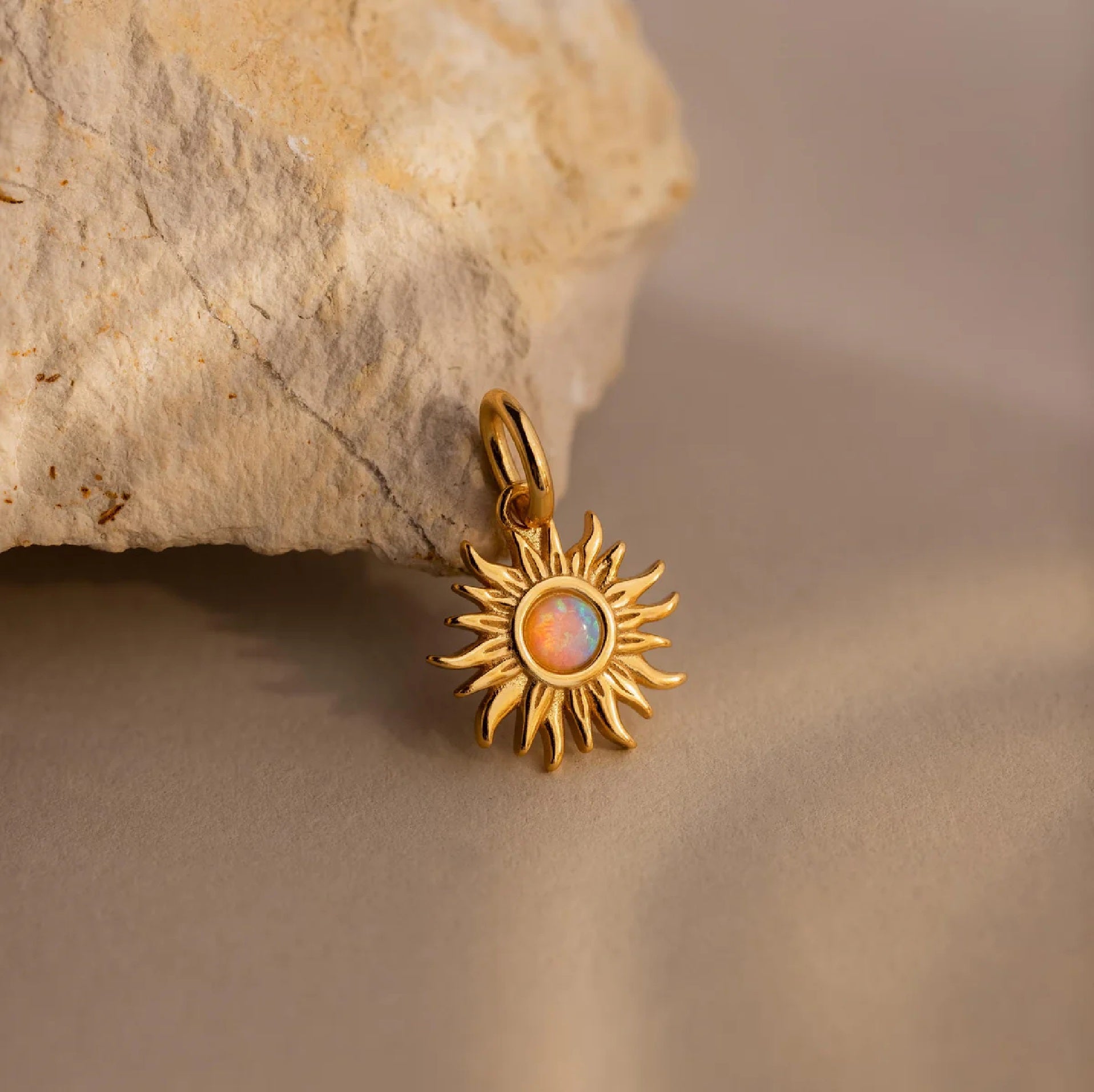 Gold sun-shaped pendant with a central gemstone on a stone surface