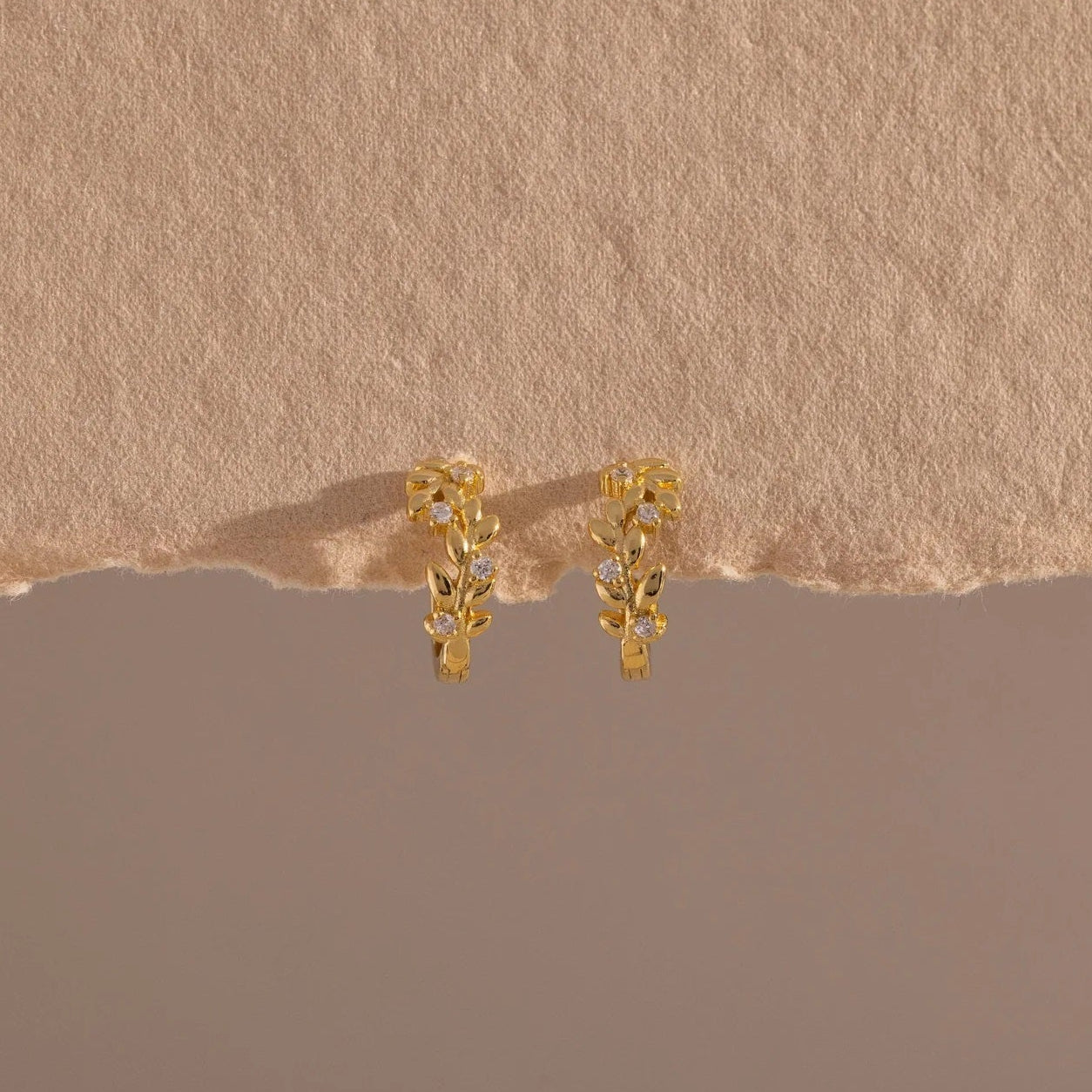 Gold earrings on a textured beige surface