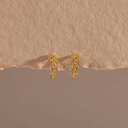 Gold earrings on a textured beige surface