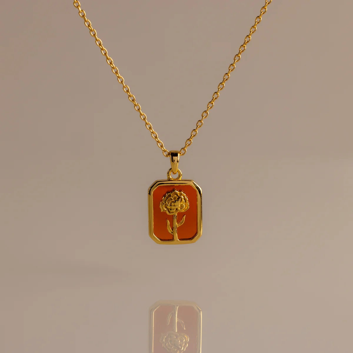 Gold necklace with a rectangular pendant featuring a rose design on a beige background