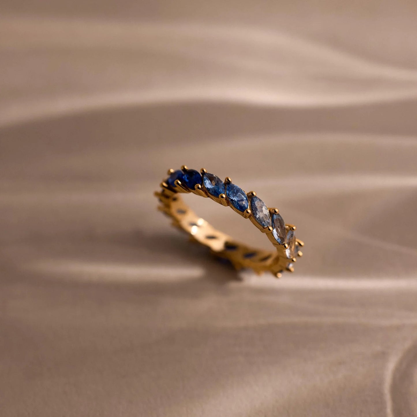 Gold ring with blue gemstones on a beige fabric background