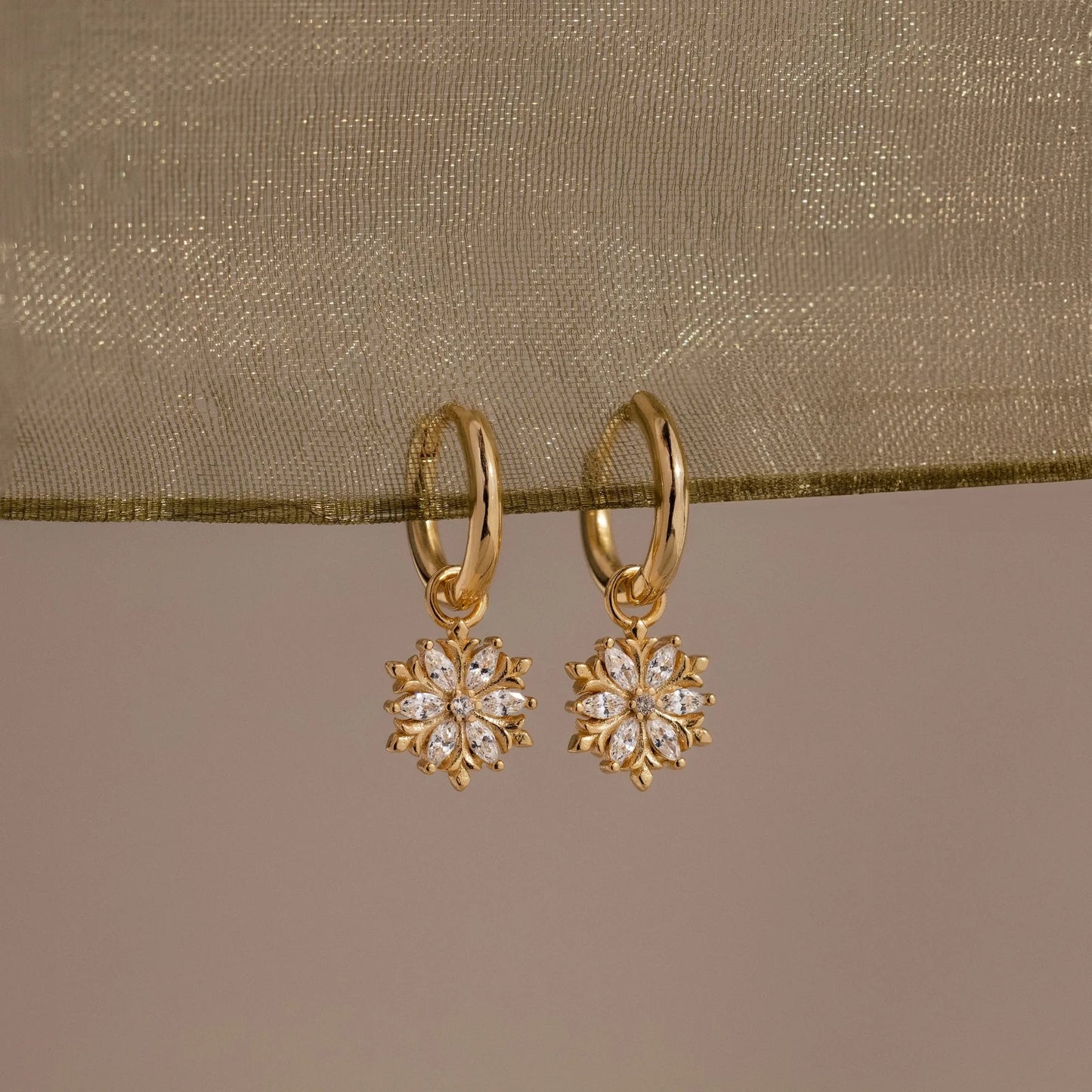 Gold earrings with floral designs on a beige fabric background