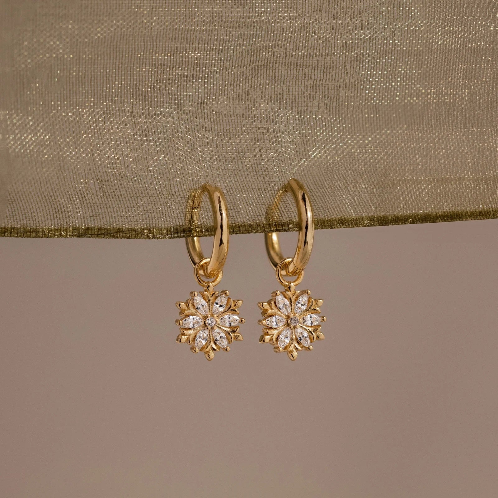 Gold earrings with floral designs on a beige fabric background