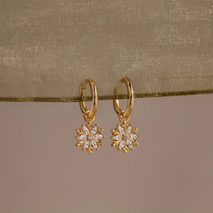 Gold earrings with floral designs on a beige fabric background