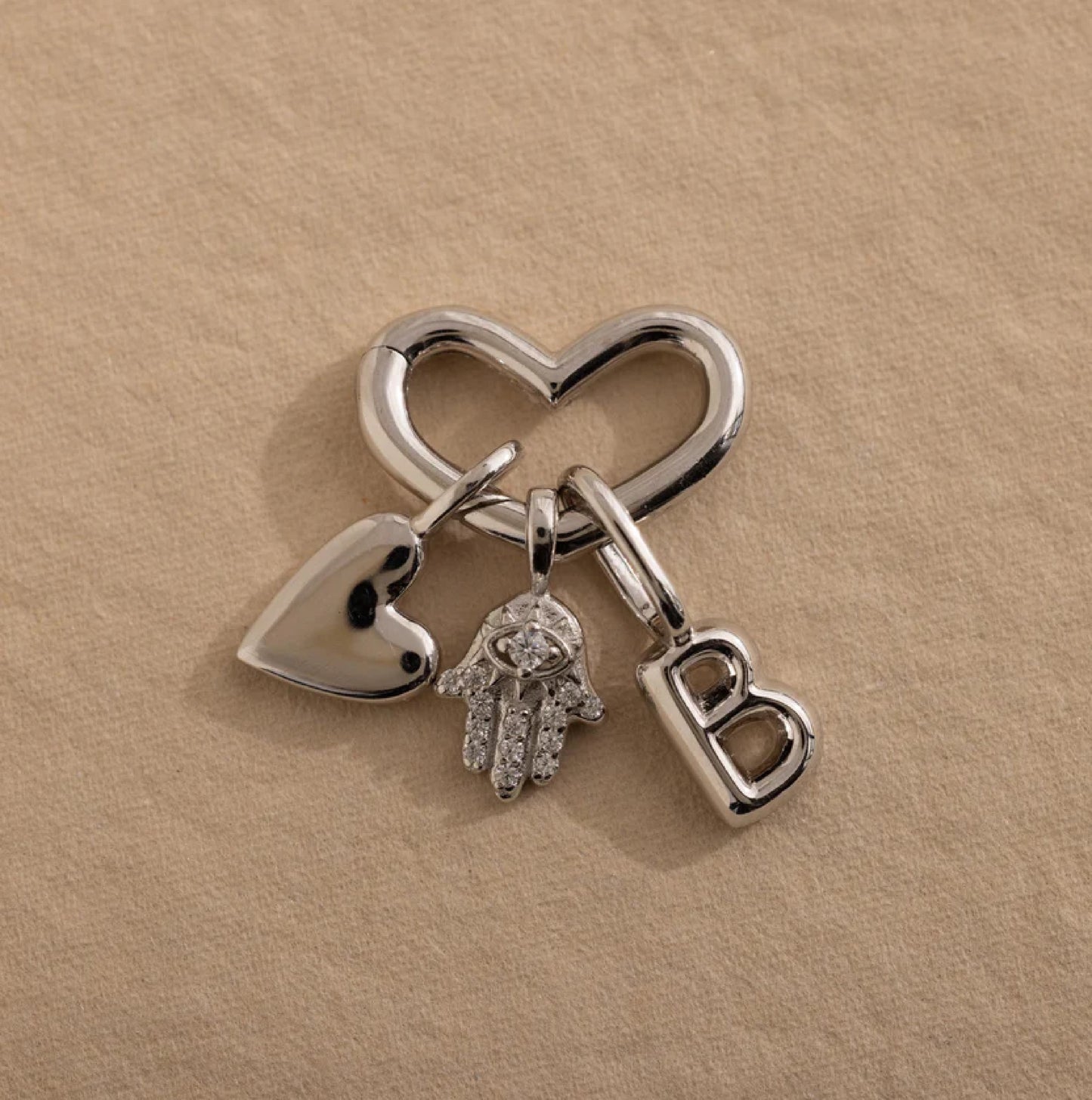Silver keychain with heart, hand, and 'B' charm on a beige background