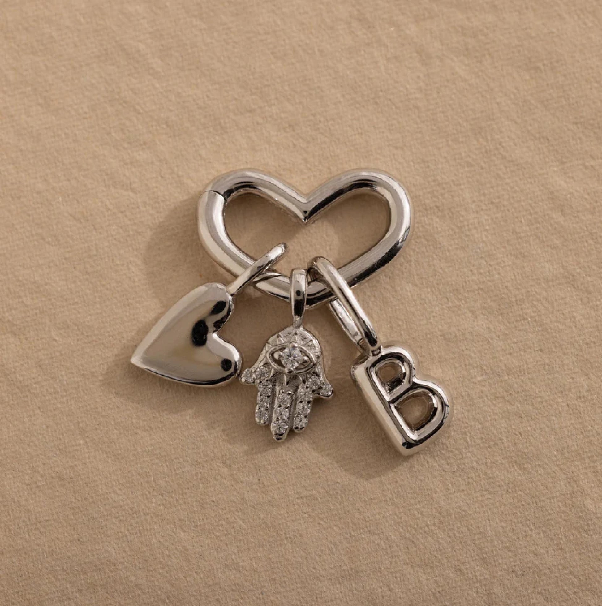 Silver keychain with heart, hand, and 'B' charm on a beige background