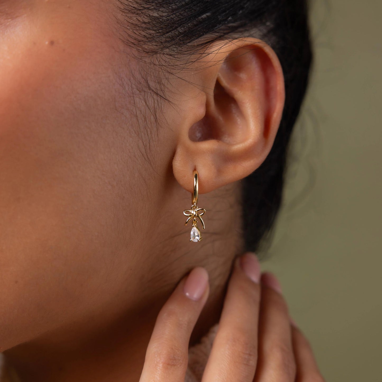 Close-up of a person wearing a gold earring with a clear gemstone.