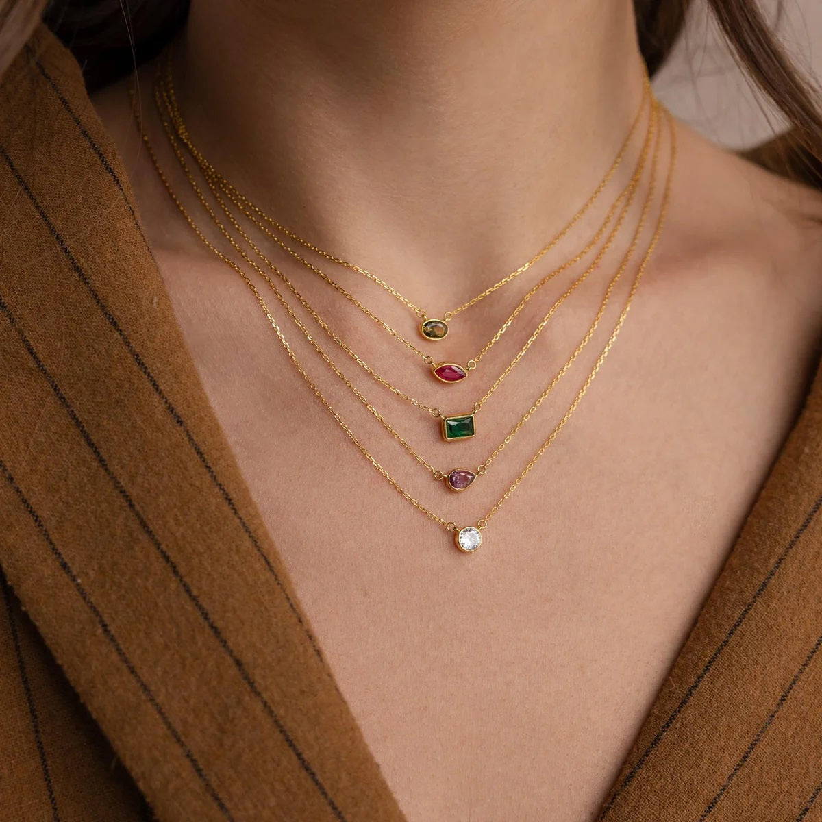 Gold necklaces with gemstones on a person wearing a brown coat