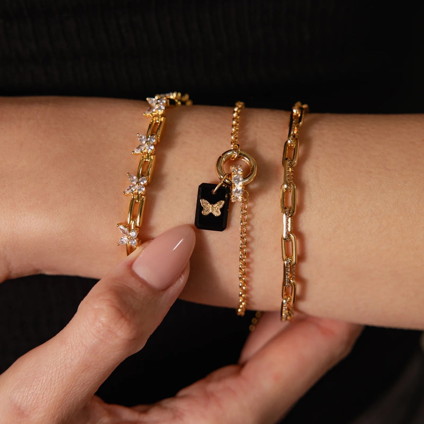 Close-up of a wrist wearing three gold bracelets with various designs on a black background