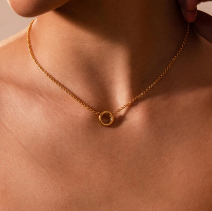 Gold necklace with a small round pendant on a person's neck against a neutral background