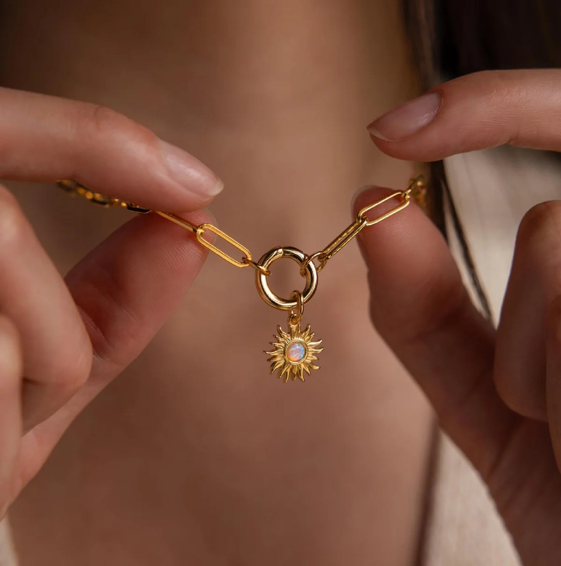 Gold bracelet with a sun charm held by hands against a neutral background