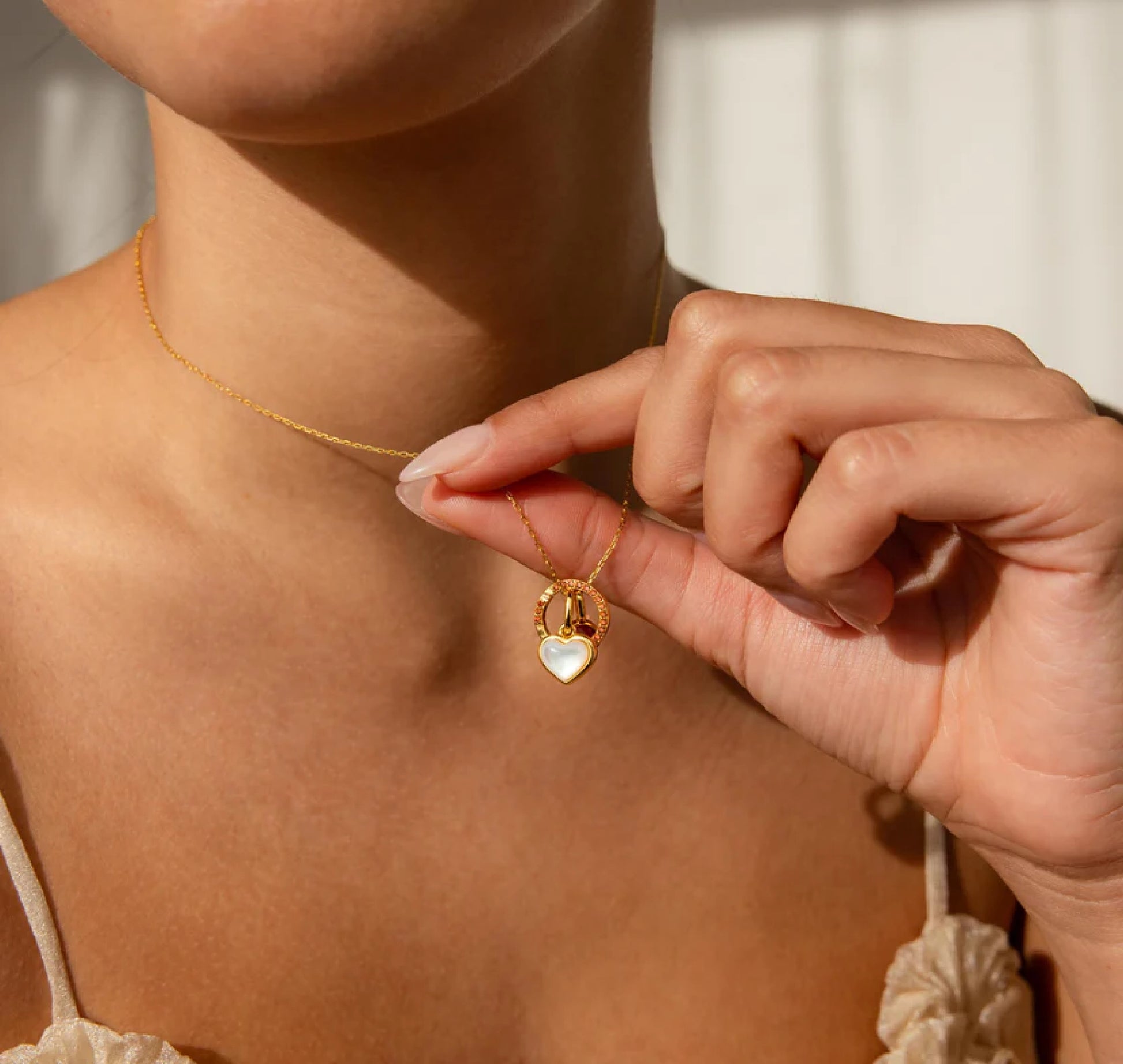 Person wearing a gold necklace with a heart-shaped pendant, held by a hand.