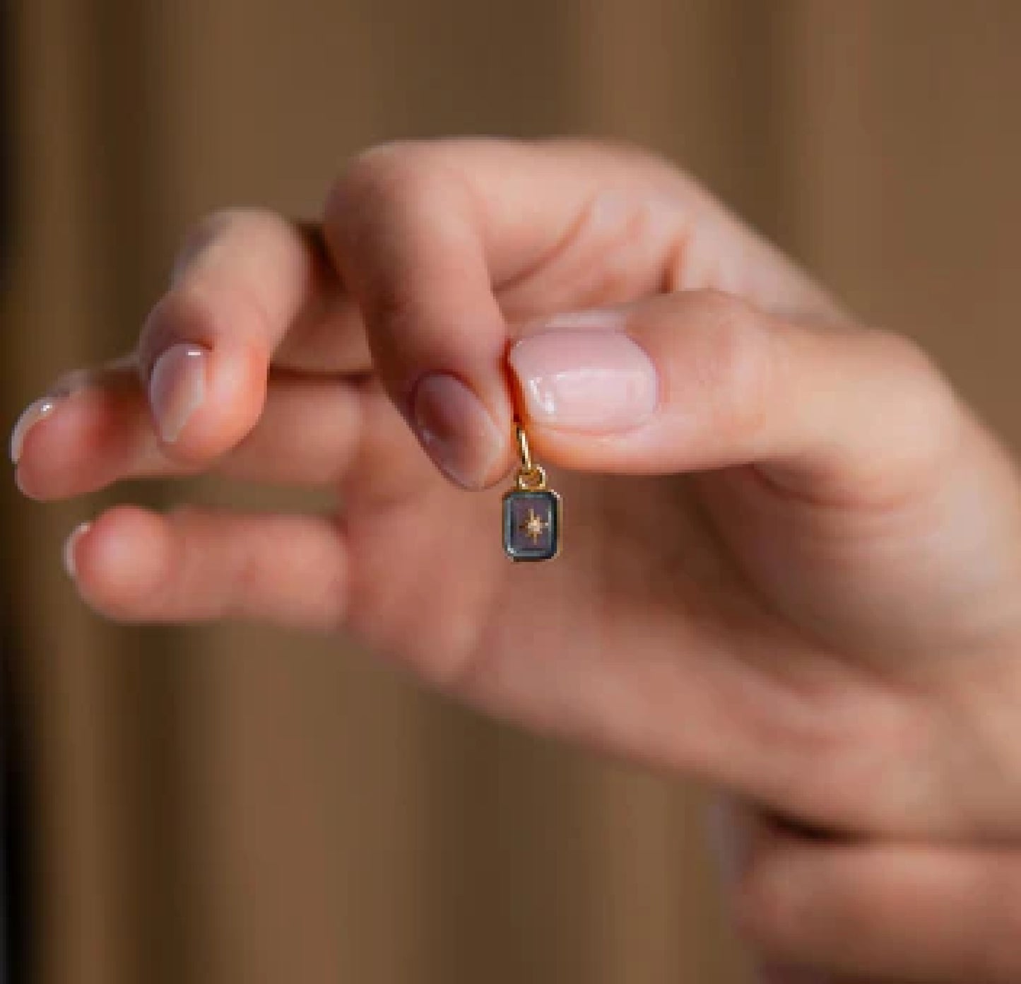 Hand holding a gold earring with a dark gemstone against a blurred background