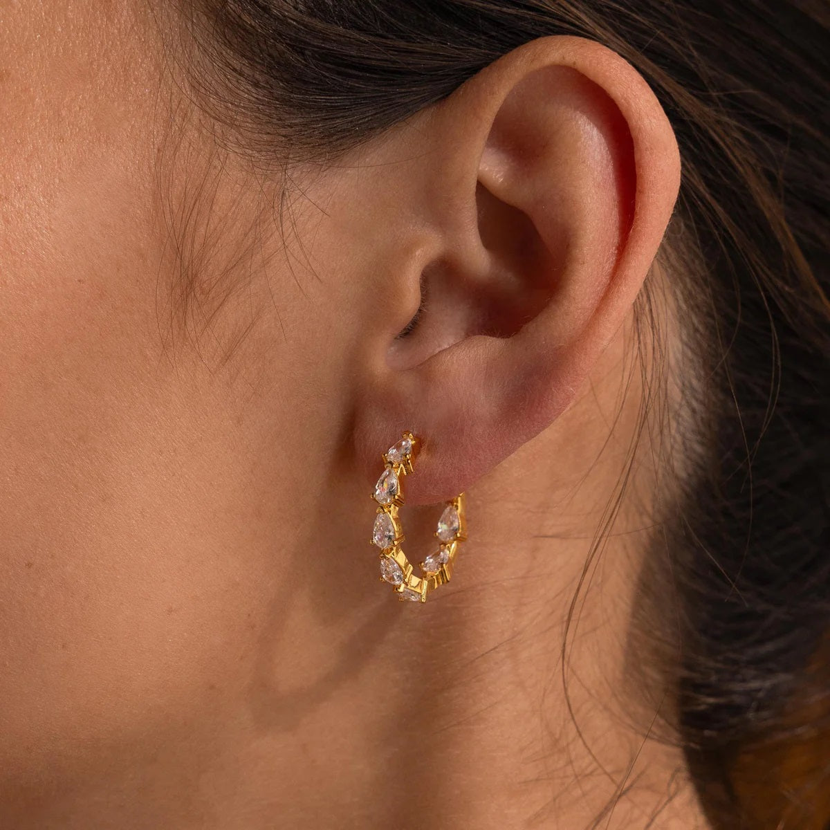 Gold hoop earrings with clear stones worn by a person.