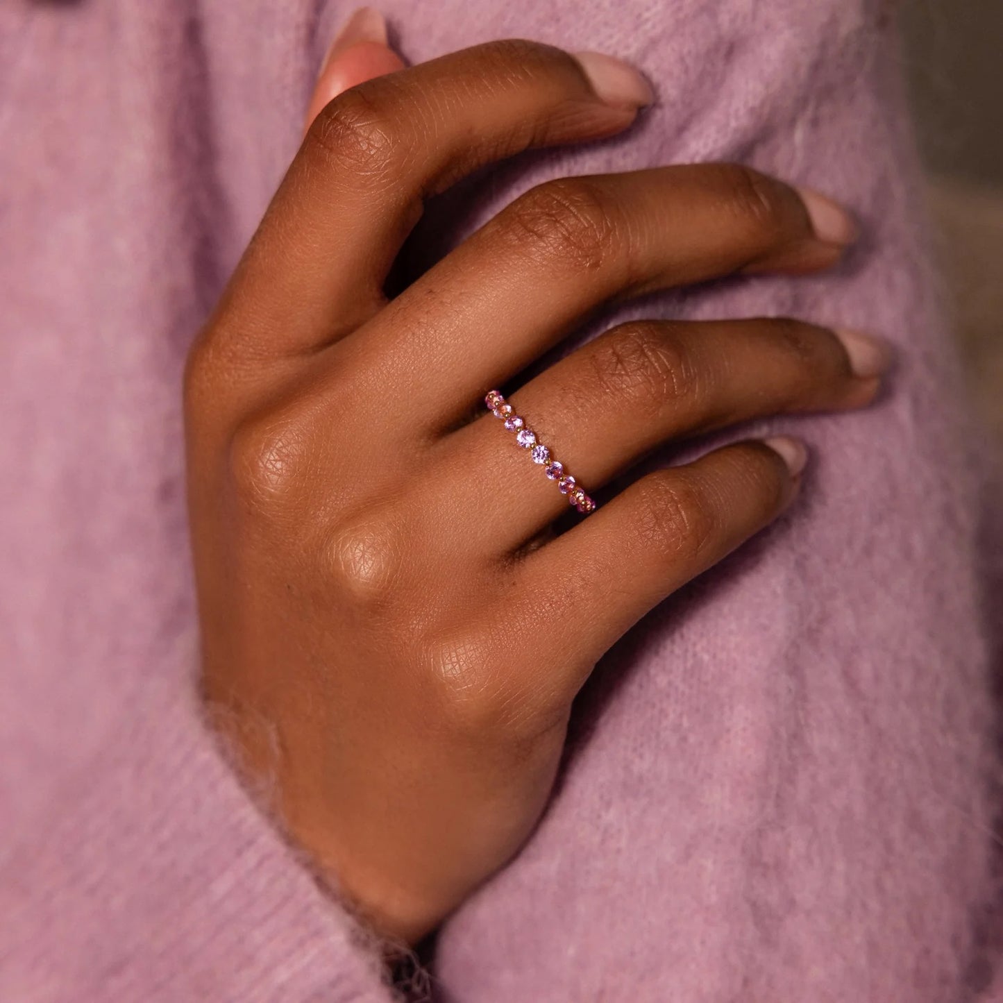 Hand wearing a pink gemstone ring against a pink background