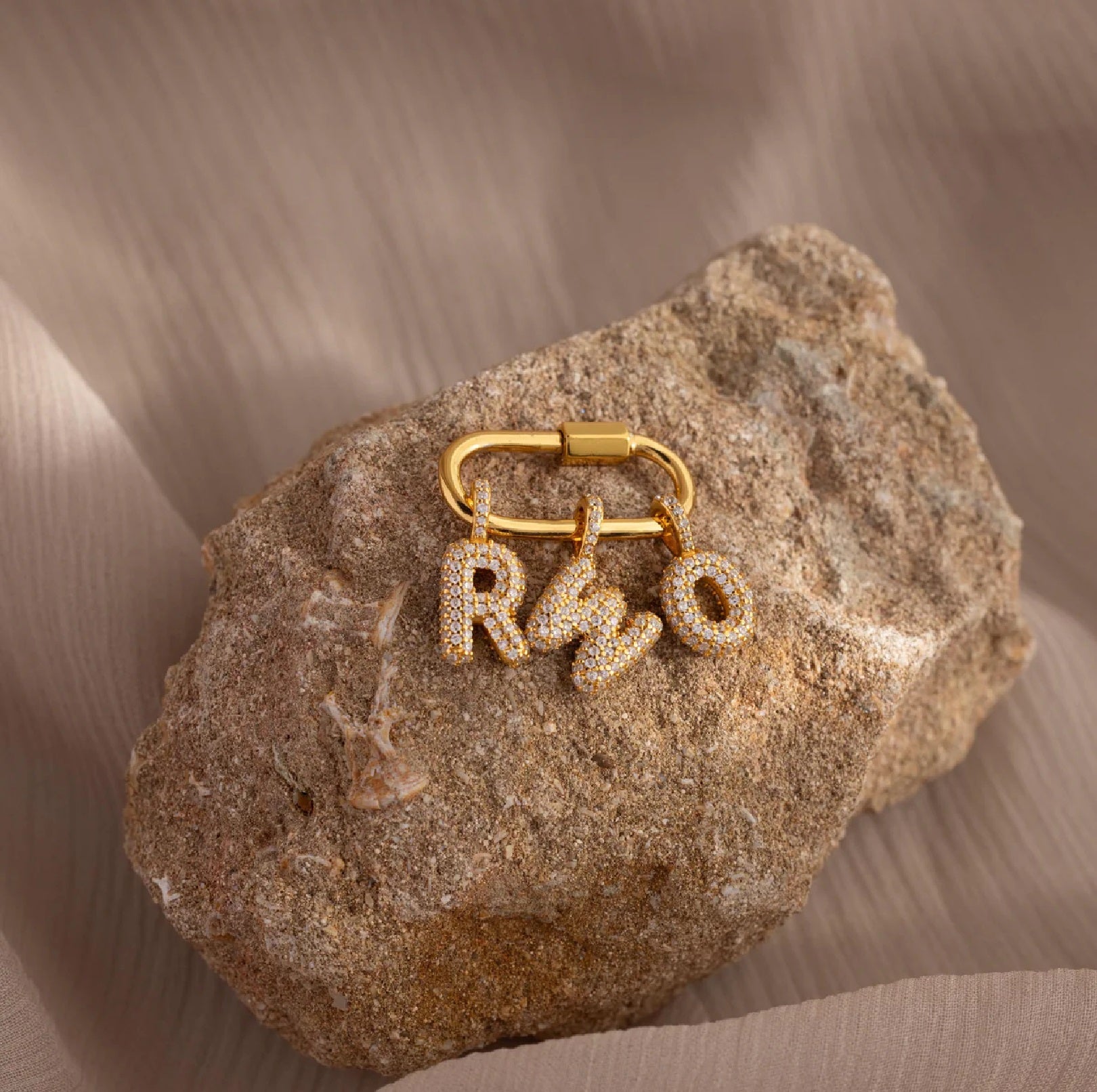 Gold keychain with 'RMO' letters on a textured stone surface