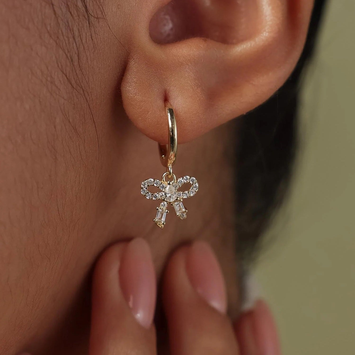Close-up of an ear wearing a gold earring with a small diamond pendant, against a neutral background.