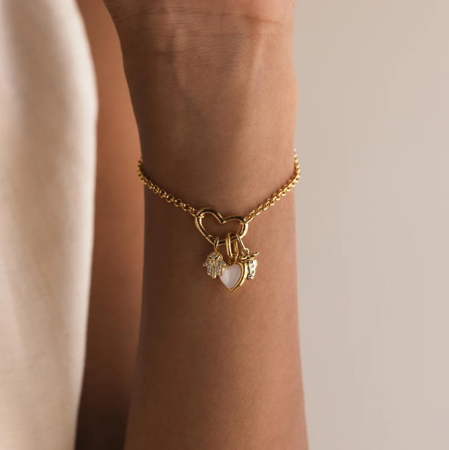 Gold bracelet with heart-shaped charm on a wrist against a neutral background