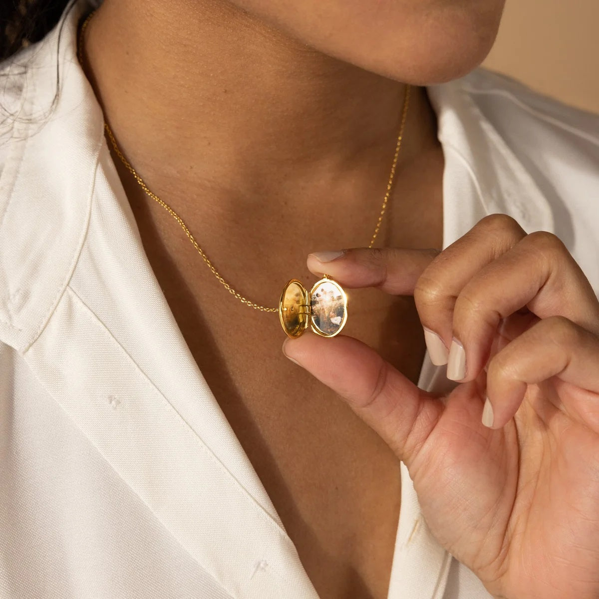 Gold necklace being held by a hand against a neutral background