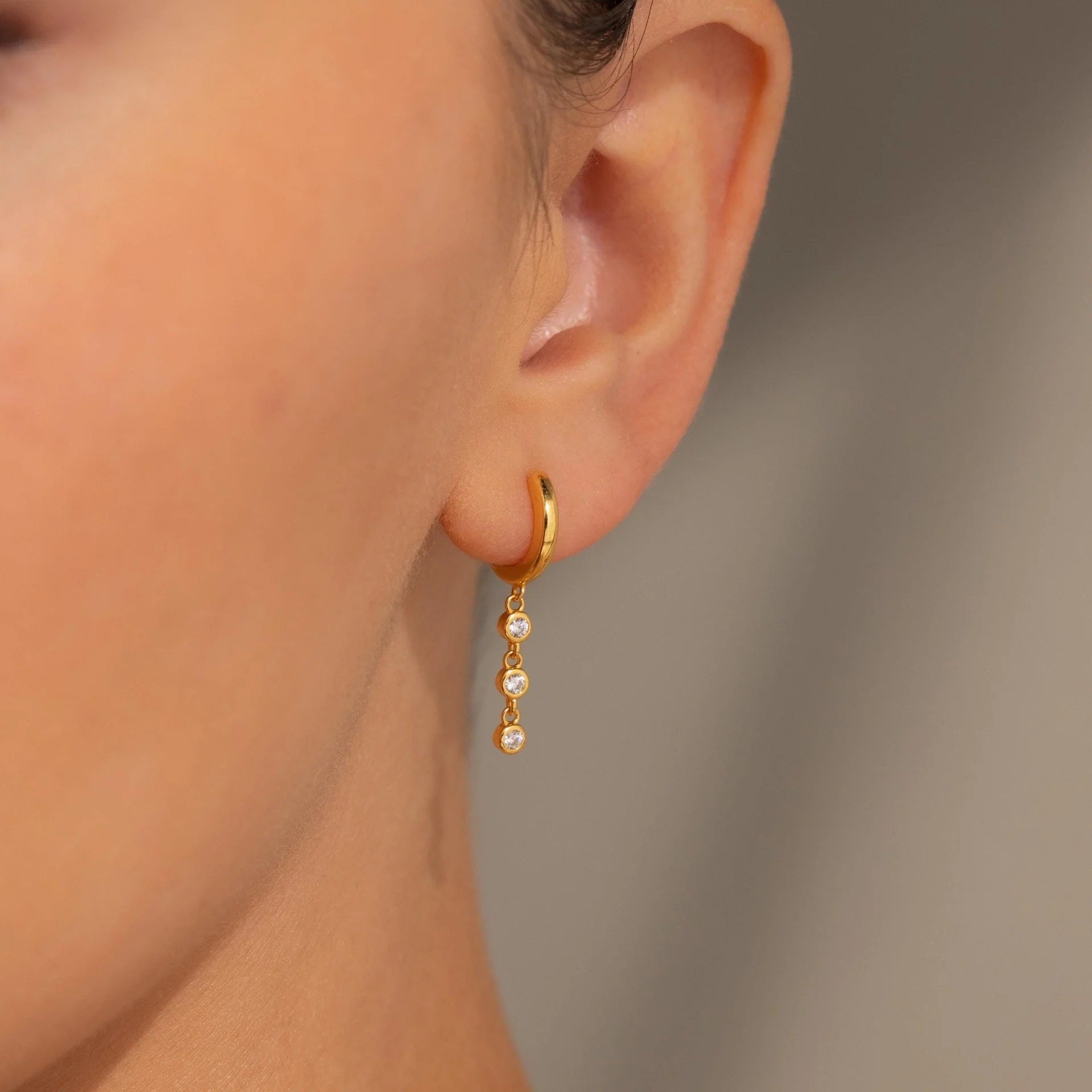 Gold hoop earring with pearl drops worn by a person against a neutral background
