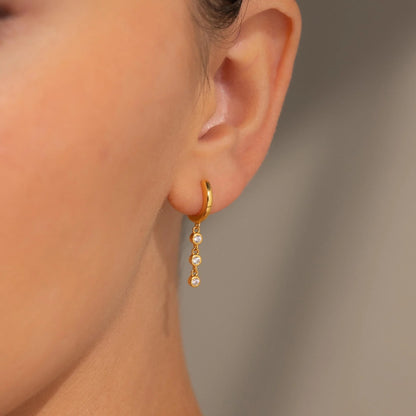 Gold hoop earring with pearl drops worn by a person against a neutral background
