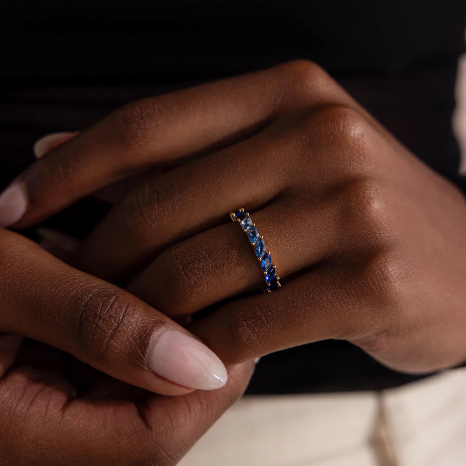 Close-up of a hand wearing a ring with blue stones on a dark background
