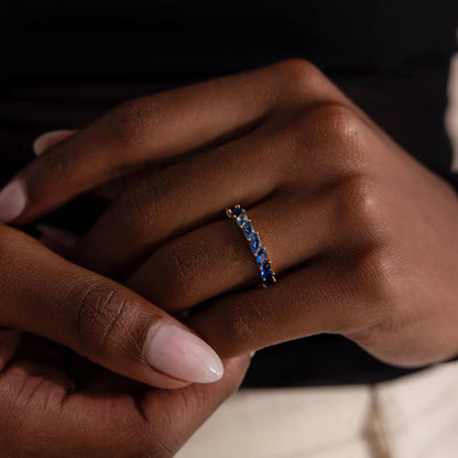 Close-up of a hand wearing a ring with blue stones on a dark background