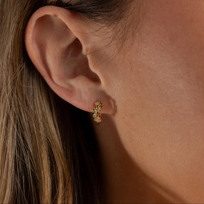 Close-up of an ear wearing a gold earring with a soft background
