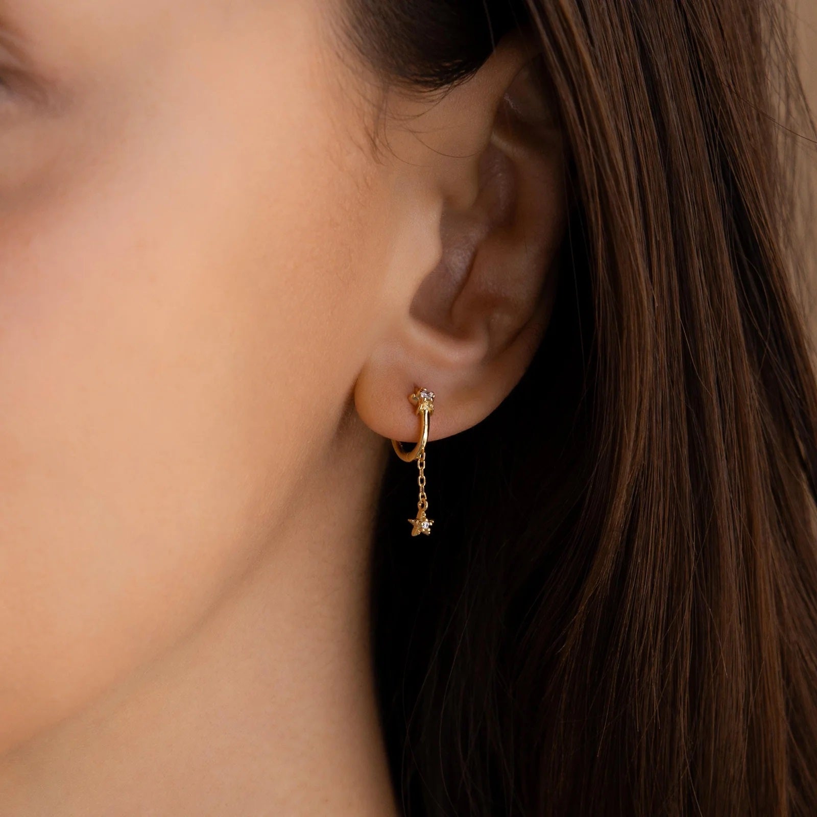 Close-up of a person wearing a gold earring with a small diamond-like stone.