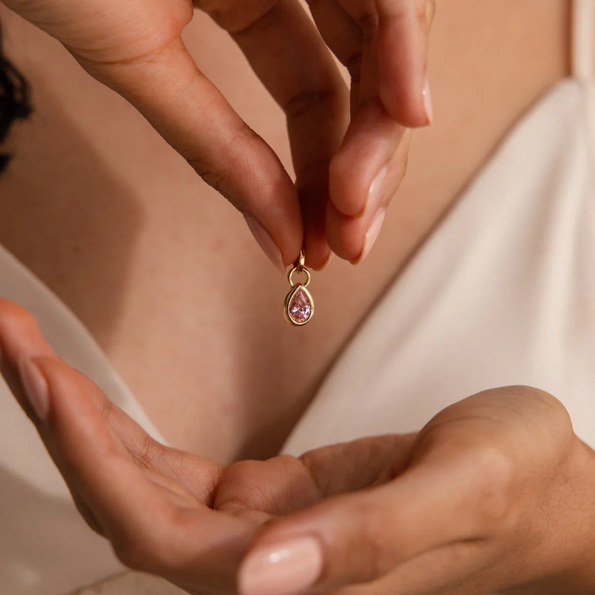 Person holding a gold teardrop-shaped earring with a pink gemstone.
