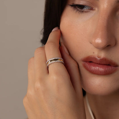 Close-up of a woman's face with hand near her ear, wearing a ring.