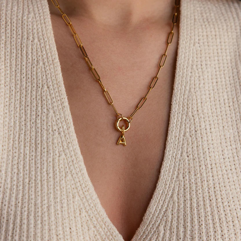 Gold necklace with a pendant worn by a person in a beige sweater.