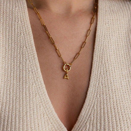 Gold necklace with a pendant worn by a person in a beige sweater.