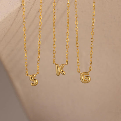 Three gold necklaces with 'S', 'K', and spiral pendants on a beige background